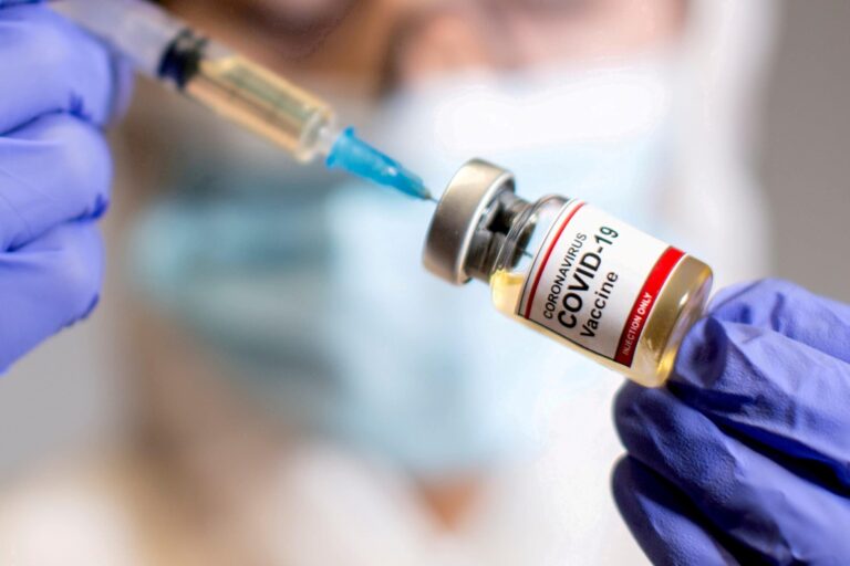 A woman holds a medical syringe and a small bottle labelled “Coronavirus COVID-19 Vaccine